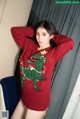 A woman wearing a red sweater with a green dinosaur on it.