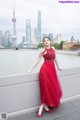 A woman in a red dress leaning against a wall.