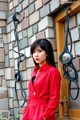 A woman in a red dress standing in front of a brick wall.