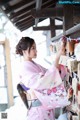 A woman in a pink kimono standing in front of a wall.