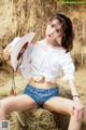 A woman in a white shirt and blue shorts sitting on a hay bale.