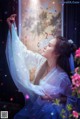 A woman in a white dress standing in front of a window.