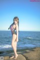 A woman in a bathing suit standing on a rock by the ocean.