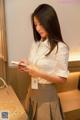 A woman in a white shirt and gray skirt looking at her phone.