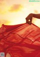 A woman's hand holding a red scarf in front of a sunset.