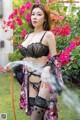 A woman in lingerie holding a hose in a garden.