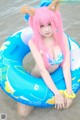 A woman with pink hair sitting on an inflatable ring in the water.