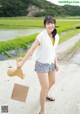 A woman standing on a dirt road holding a piece of paper.