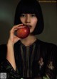 A woman holding an apple in front of her face.