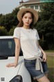 a woman wearing a white t - shirt and denim shorts leaning against a car